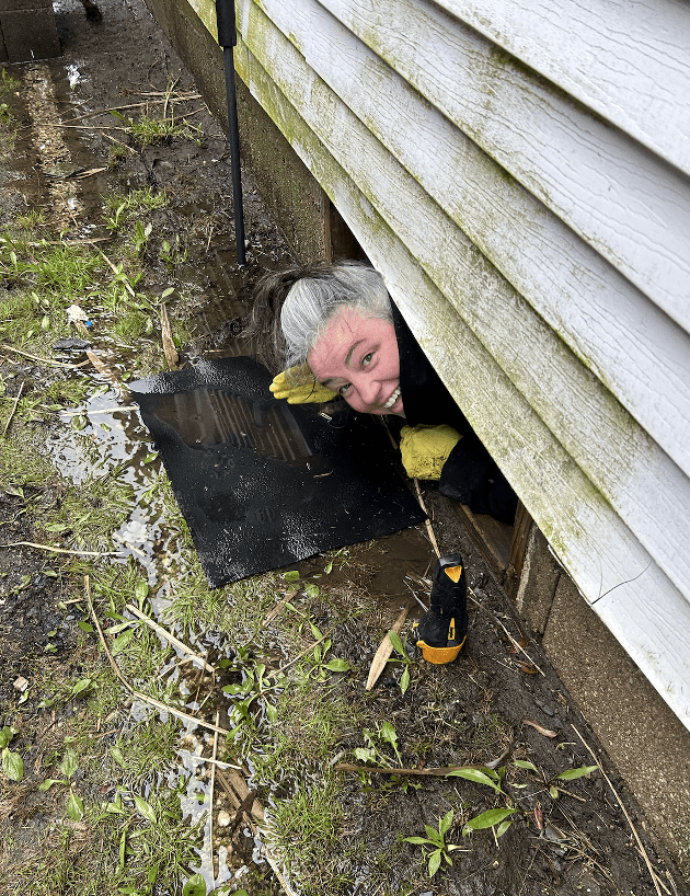 WAP Social Manager Julie Cappiello underneath her crawlspace looking for raccoons.